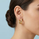 Gold hoop earrings worn by a person with a plain background