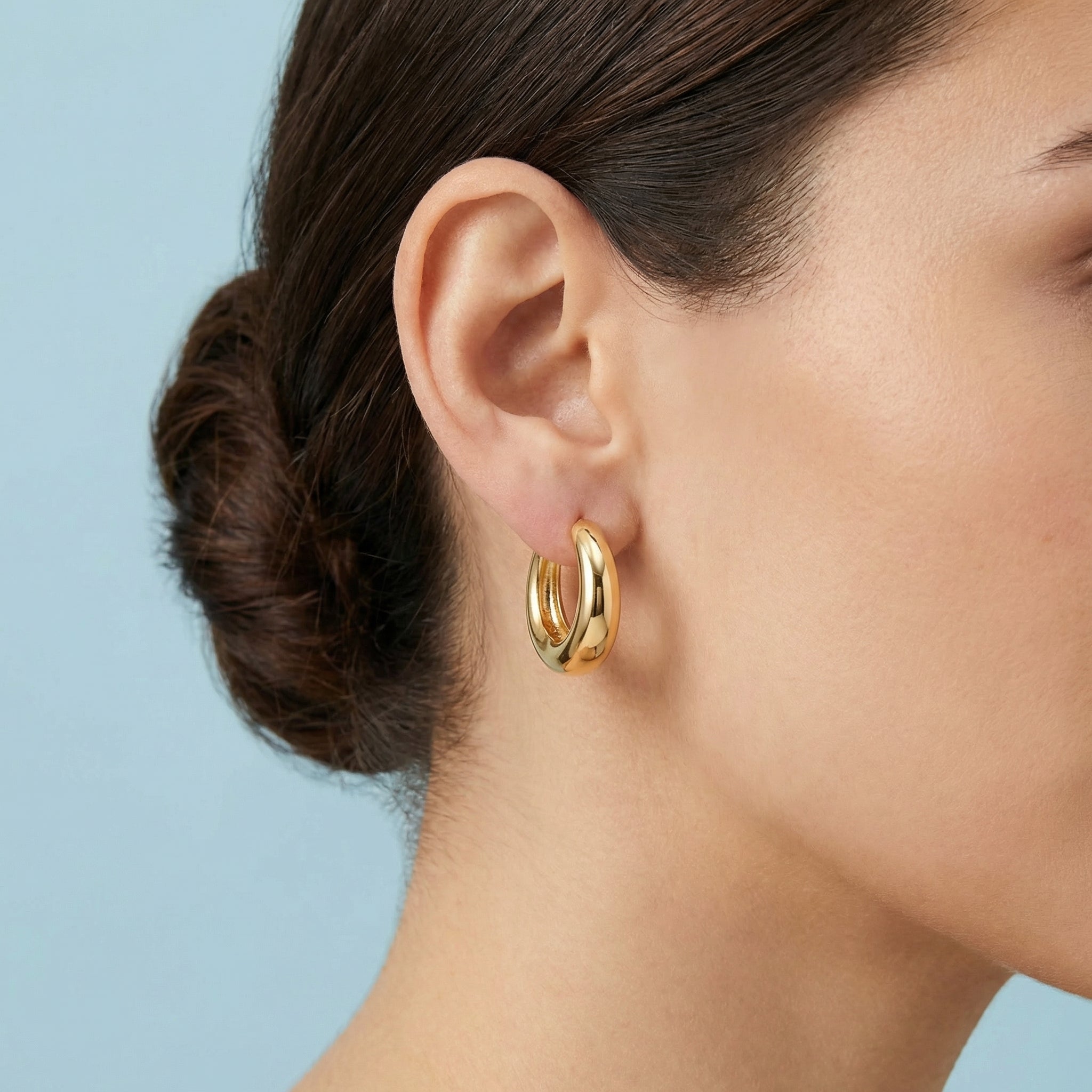 Gold hoop earrings worn by a person with a plain background